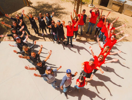 The image shows A Sense of Home volunteers with their hands up in the air while standing in a shape of a heart